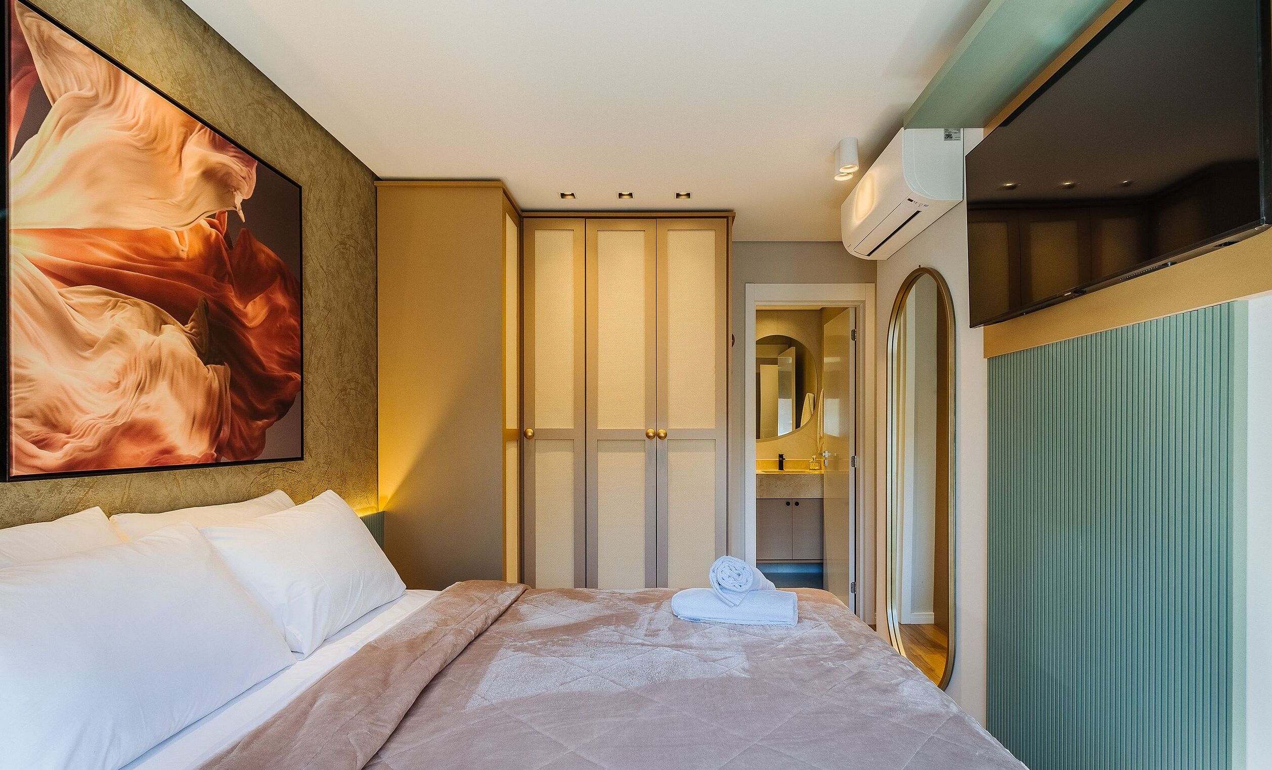 Una habitación de hotel con una cama, un cuadro grande, un armario, un espejo y un equipo de aire acondicionado.