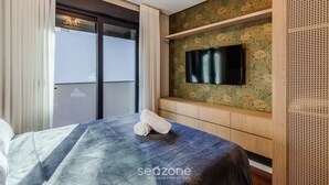 Ein Hotelzimmer mit Bett, einem an einer blumengedeckten Wand montierten Fernseher und einer Schiebetür, die auf einen Balkon führt.