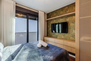 A hotel room with a bed, a TV mounted on a floral wallpapered wall, and a sliding door leading to a balcony. - Modern Apartment in Downtown Gramado Dlh0105 (Gramado)