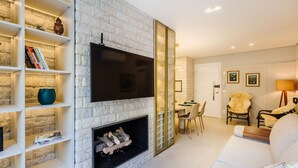 Ein modernes Wohnzimmer mit Steinwand, Flachbildfernseher, Kamin und Essbereich mit Stühlen und Tisch.
