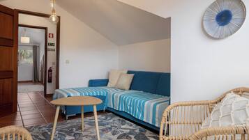 Une pièce avec un canapé bleu, une petite table ronde, des chaises en osier, un tapis à motifs et une assiette décorative accrochée au mur.
