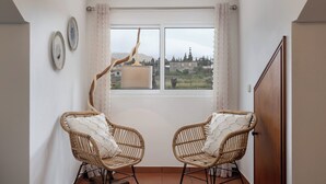 Um quarto com duas cadeiras de vime, uma janela com cortinas e vista para um edifício.