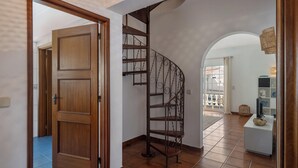 Uma porta de madeira leva a um quarto com escada em espiral e vista para uma varanda externa.