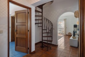Eine Holztür, die in einen Raum mit einer Wendeltreppe und Blick auf einen Außenbalkon führt.