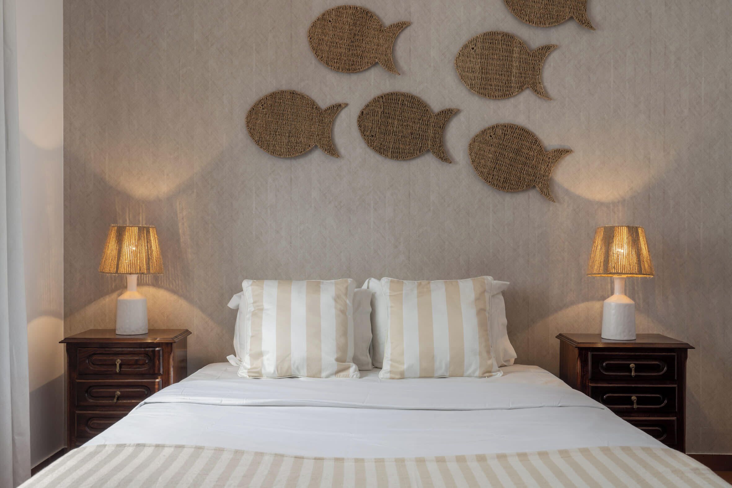 Ein Schlafzimmer mit einem Bett, zwei Nachttischen, zwei Lampen und Wanddekorationen mit Fischen.