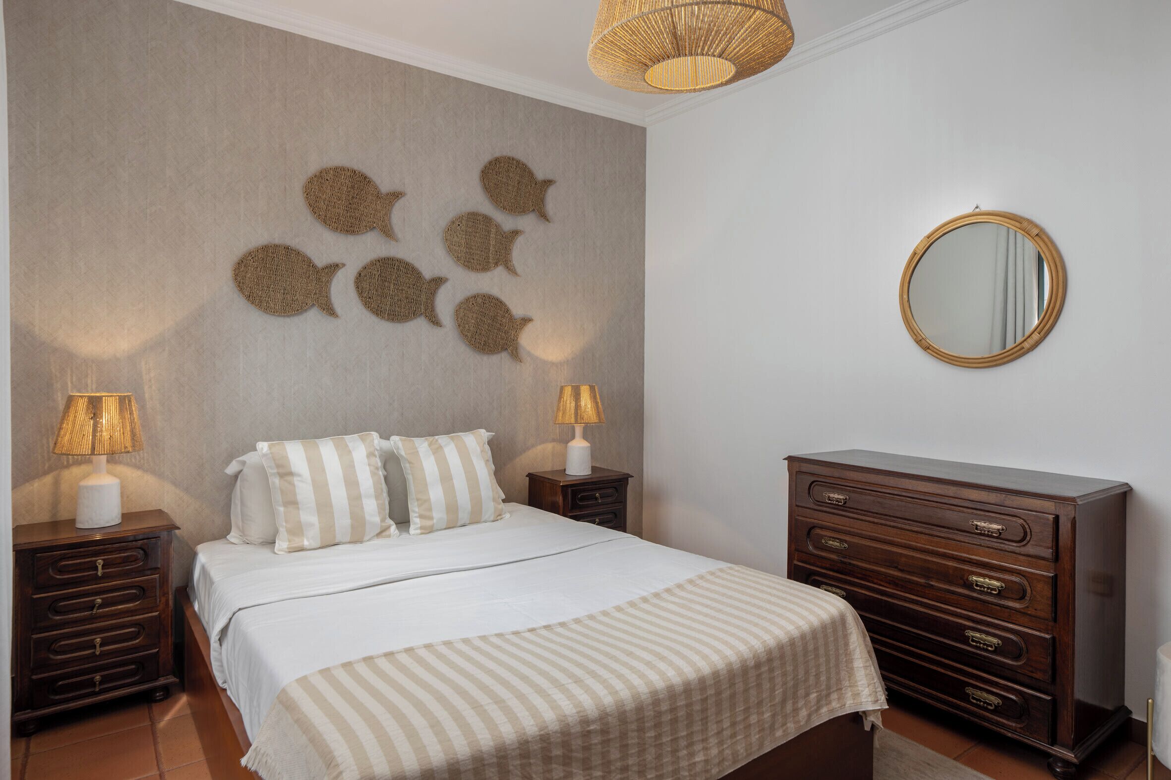Un dormitorio con una cama, dos mesitas de noche, un aparador, un espejo en la pared y decoración mural.
