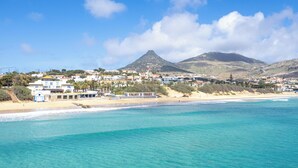 Uma vila costeira com edifícios à beira da praia, águas turquesa cristalinas e uma montanha ao fundo.