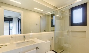 Un baño moderno con ducha envuelta en vidrio, un espejo grande y un lavamanos blanco.