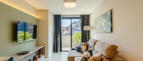 A modern living room with a flat-screen TV, a sofa with cushions, a floor lamp, and a painting on the wall.