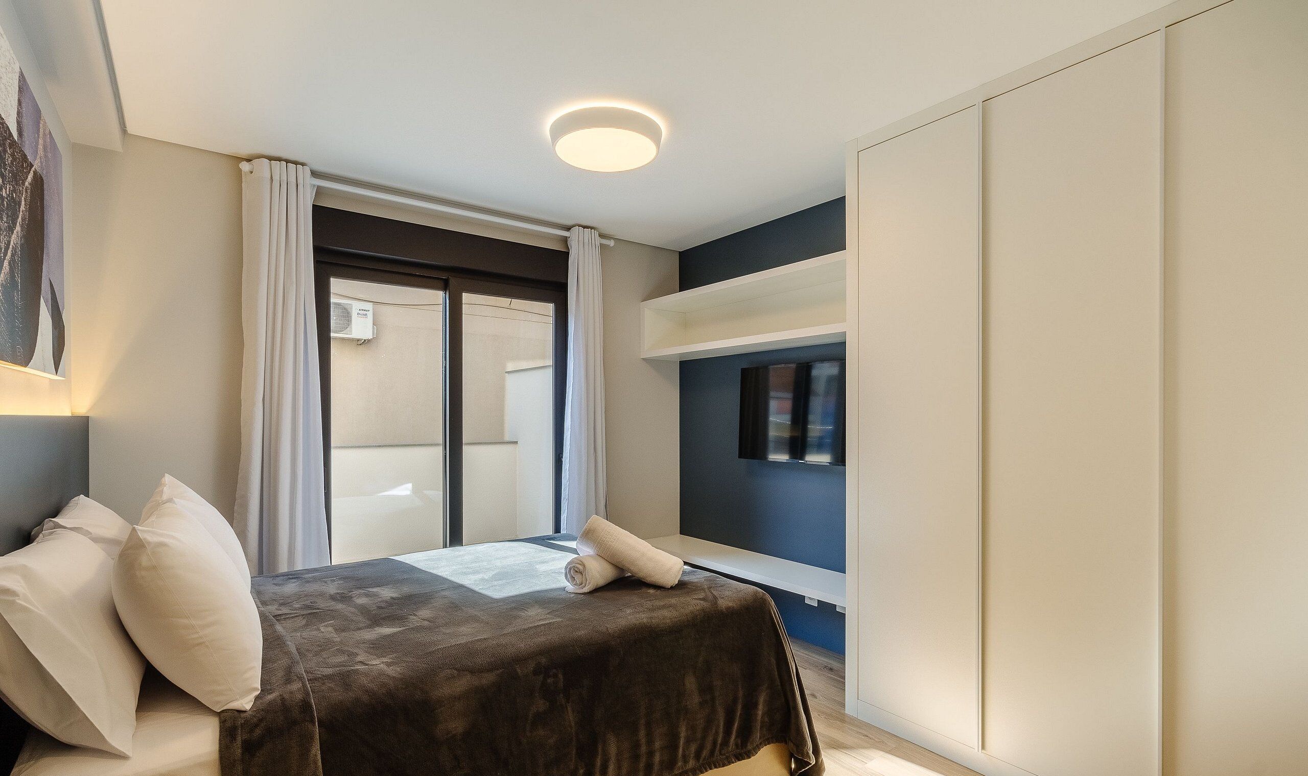 Un dormitorio con cama, ventana y luz de techo.