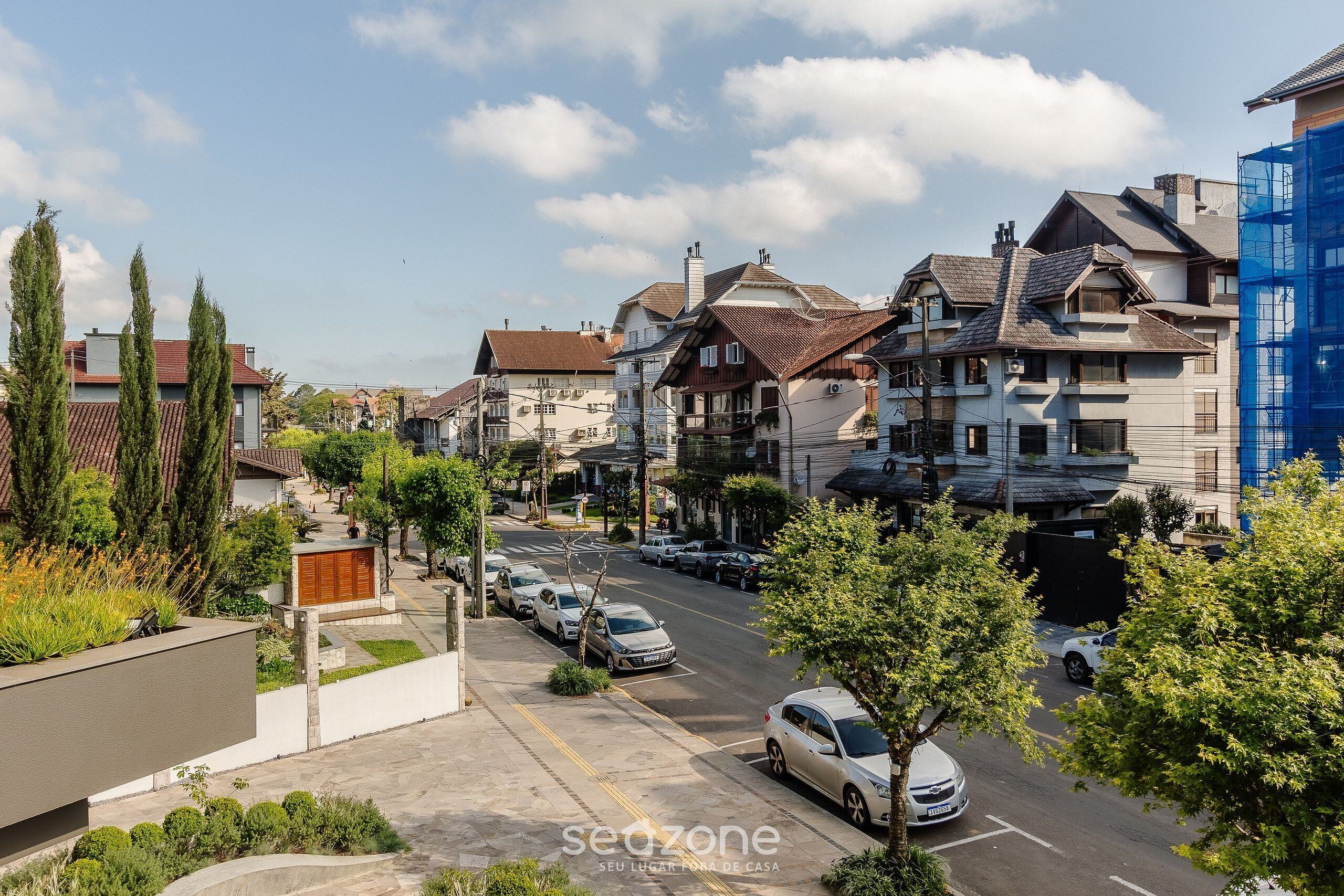 A residential street with houses, parked cars, and trees.