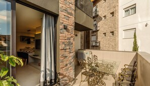 Un apartamento moderno con puerta de cristal que da a un comedor, un balcón con mobiliario de metal ornamentado y fachada de piedra.