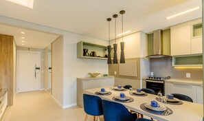 Una cocina moderna con comedor, que incluye una mesa larga preparada para cuatro personas, horno empotrado e iluminación colgante.