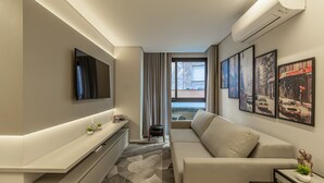Ein modernes Hotelzimmer mit Fernseher, einer Couch, einem kleinen Tisch mit Dekoration und gerahmten Kunstwerken an den Wänden.