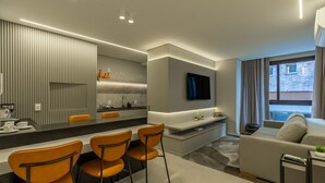 Ein modernes Wohnzimmer mit einer Couch, einem Essbereich mit Stühlen, einer Küche mit einer Arbeitsfläche und einem an der Wand befestigten Fernseher.