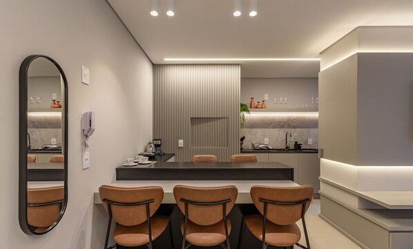 Una habitación de hotel moderna con comedor, un espejo grande y una encimera de cocina.