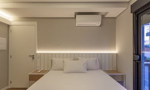 Habitació d'hotel amb un llit, taules de nit, aire condicionat fixat a la paret i una porta.