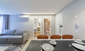 A modern hotel room with a sofa, dining table, chairs, and a view into the bathroom. - Modern Apartment in the Center of Gramado Dlh0206 (Gramado)