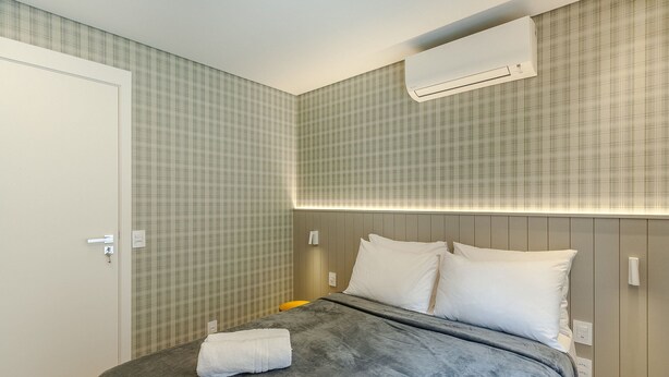 Een hotelkamer met een bed, een witte handdoek, een wandairconditioner en een deur.