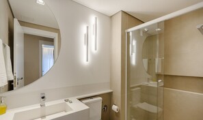 Un baño moderno con un espejo grande, cabina de ducha de vidrio y lavamanos blanco.