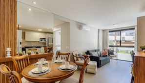 A modern living room with a dining area, featuring a wooden dining table set for four, a sofa, and a large window offering a view of the outside. - Charming Apartment in Gramado Dlh0205 (Gramado)