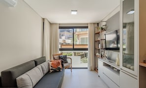 A modern living room with a sofa, a TV mounted on the wall, and a view of the outside. - Charming Apartment in Gramado Dlh0205 (Gramado)