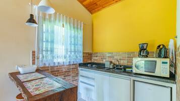 Une cuisine avec un mur en briques, un plafond en bois, un mur jaune, un plan de travail blanc, une cuisinière, un four à micro-ondes, une machine à café et une table avec un set de table.