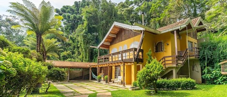 A two-story house with a balcony, surrounded by lush greenery.