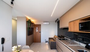 A modern kitchen with a built-in microwave, a stove, and a sink. There is a wooden cabinet above the stove and a plant hanging on the wall. - Strategic Apt, Jardim Goias - Tho2707 (Goiânia)