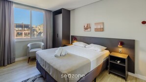 Ett modernt hotellrum med en stor säng, en stol, ett nattduksbord och utsikt över stadsbilden.
