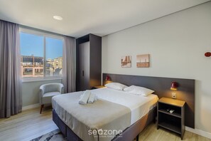 A modern hotel room with a large bed, a chair, a nightstand, and a view of the cityscape. - Studio in the Historic Center Near Ccmq Tco0512 (Porto Alegre)