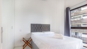 A hotel room with a bed, a small wooden chair, a window with a view of buildings, and a curtain. - Luxury Beachfront Apt in Boa Viagem - Iaa1003 (Recife)