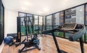 Ein Fitnessstudio mit Trainingsgeräten, Laufband und großen Fenstern mit Blick auf Gebäude.