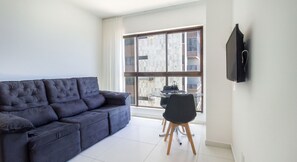 Ein modernes Wohnzimmer mit einem dunkelgrauen Sofa, einem kleinen runden Tisch und einem an der Wand befestigten Fernseher.