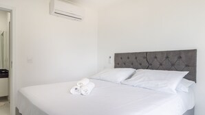 A hotel room with a bed, white linens, a grey headboard, and a wall-mounted air conditioner. - Comfortable Seaside Apt in Boa Viagem Iaa0502 (Recife)