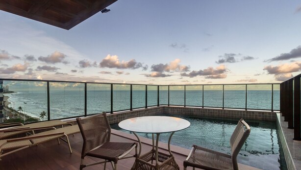 A balcony with a glass railing, a pool table, and wicker chairs. - Comfortable Seaside Apt in Boa Viagem Iaa0502 (Recife)