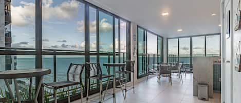 A spacious balcony with a view of the sea, furnished with chairs and tables.