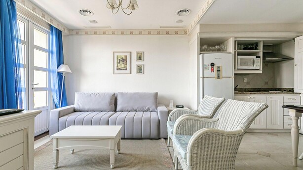A living room with a sofa, a coffee table, and a wicker chair. There is a kitchen area with a refrigerator and microwave. - Beautiful Penthouse Luxury Resort Jurere Ilc2505 (Florianópolis)