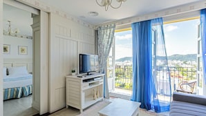 A hotel room with a bed, a TV, a sofa, a balcony with blue curtains, and a city view. - Beautiful Penthouse Luxury Resort Jurere Ilc2505 (Florianópolis)