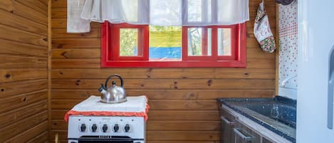 Una cocina compacta con estufa blanca, hervidor y ventana con marcos rojos.