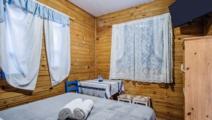Habitación de cabaña de madera con una cama, una mesa y dos ventanas con cortinas.