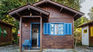 Una cabaña de madera con un porche, una mesita y una puerta que da al interior.