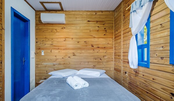 Una habitación de cabaña de madera con una cama, almohadas, una puerta azul y una ventana con cortinas.