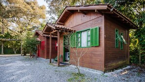 Una cabaña de madera con porche y una pequeña construcción adosada, rodeada de árboles.