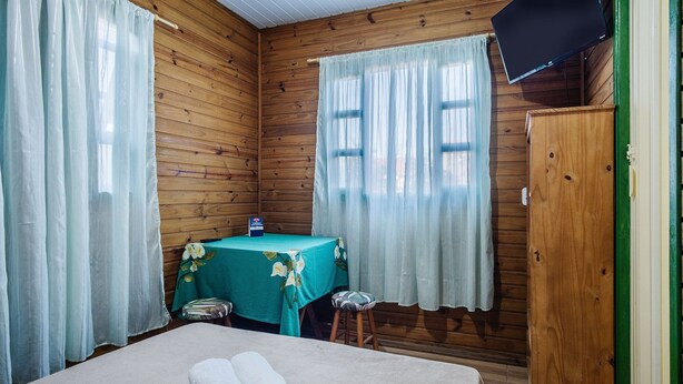 Una habitación de madera con una cama, una mesa con mantel floral y un televisor en la pared.