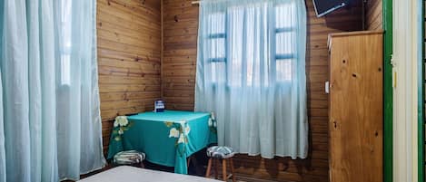 Una habitación de madera con una cama, una mesa con mantel floral y un televisor en la pared.