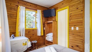 Ett rum med träpanel, en säng, ett bord, en tv som är monterad på väggen och ett fönster med gardiner.