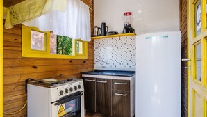 A compact kitchen with a gas stove, a white refrigerator, and a tiled backsplash. - Cabin Between Lagoon and Praia do Rosa - Prj004 (Imbituba)