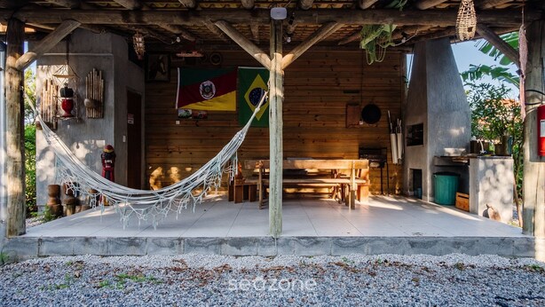 A wooden cabin with a hammock, a Brazilian flag, and a rustic interior. - Cabin Between Lagoon and Praia do Rosa - Prj004 (Imbituba)
