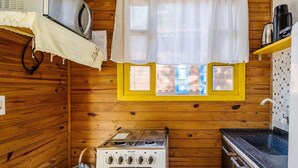 A compact kitchen with a stove, a sink, and a window with curtains. - Cabin Between Lagoon and Praia do Rosa - Prj004 (Imbituba)